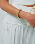 Gia Mega Bangle in Gold on wrist with white outfit