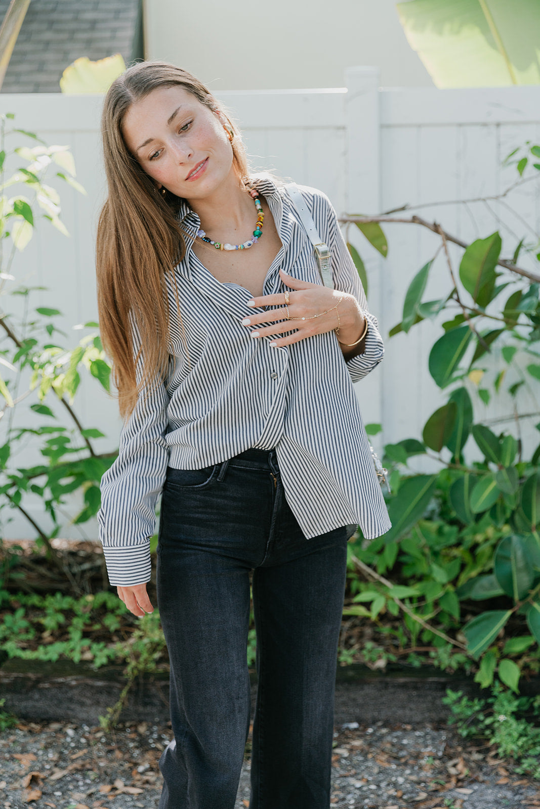 Woman wearing Aris Shirt in Solene Stripe black pants standing outdoors with greenery in the background front view