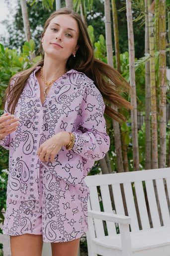Woman wearing a pink paisley outfit standing outdoors with greenery in the background