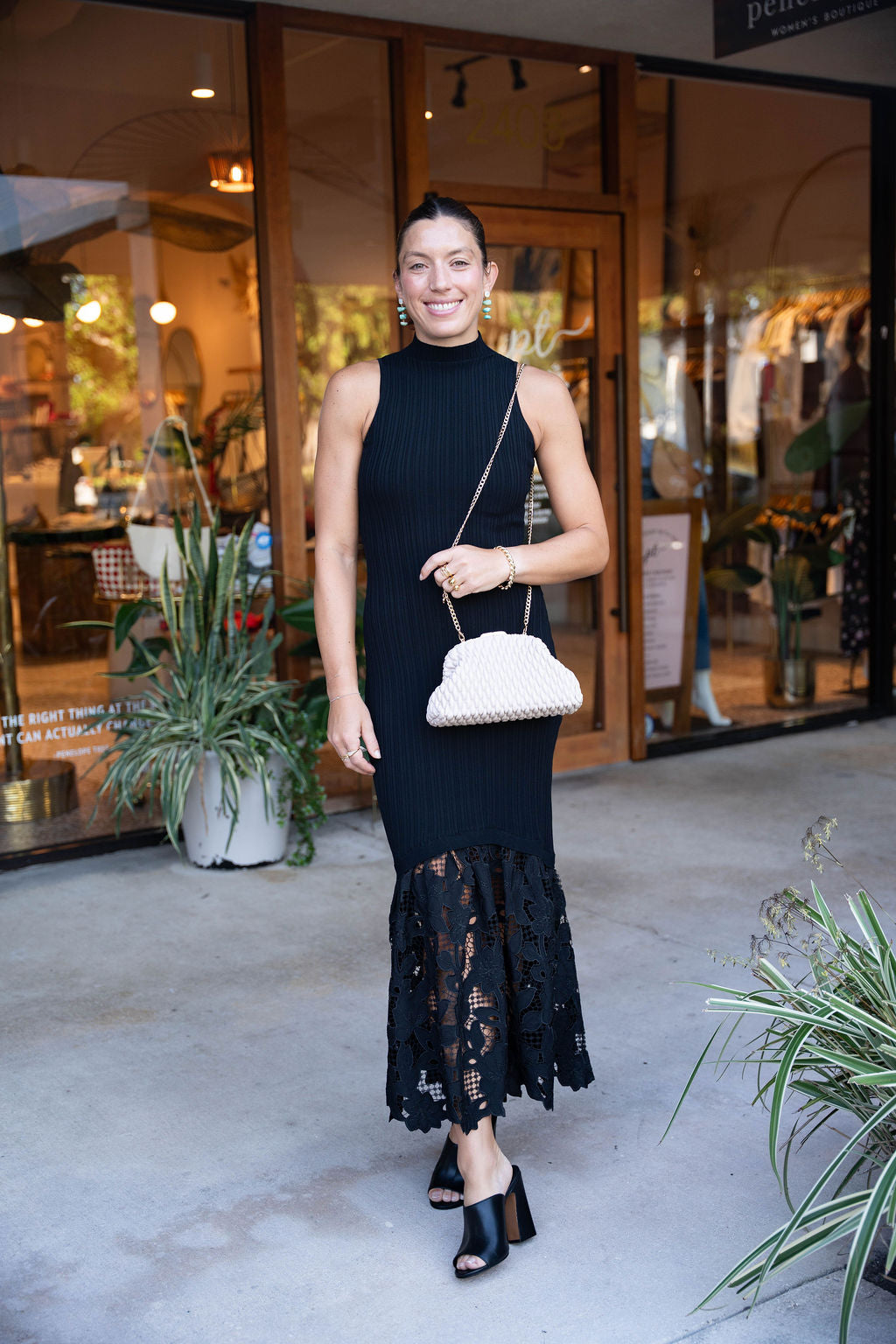 Woman in a black dress with lace details standing outside a store.