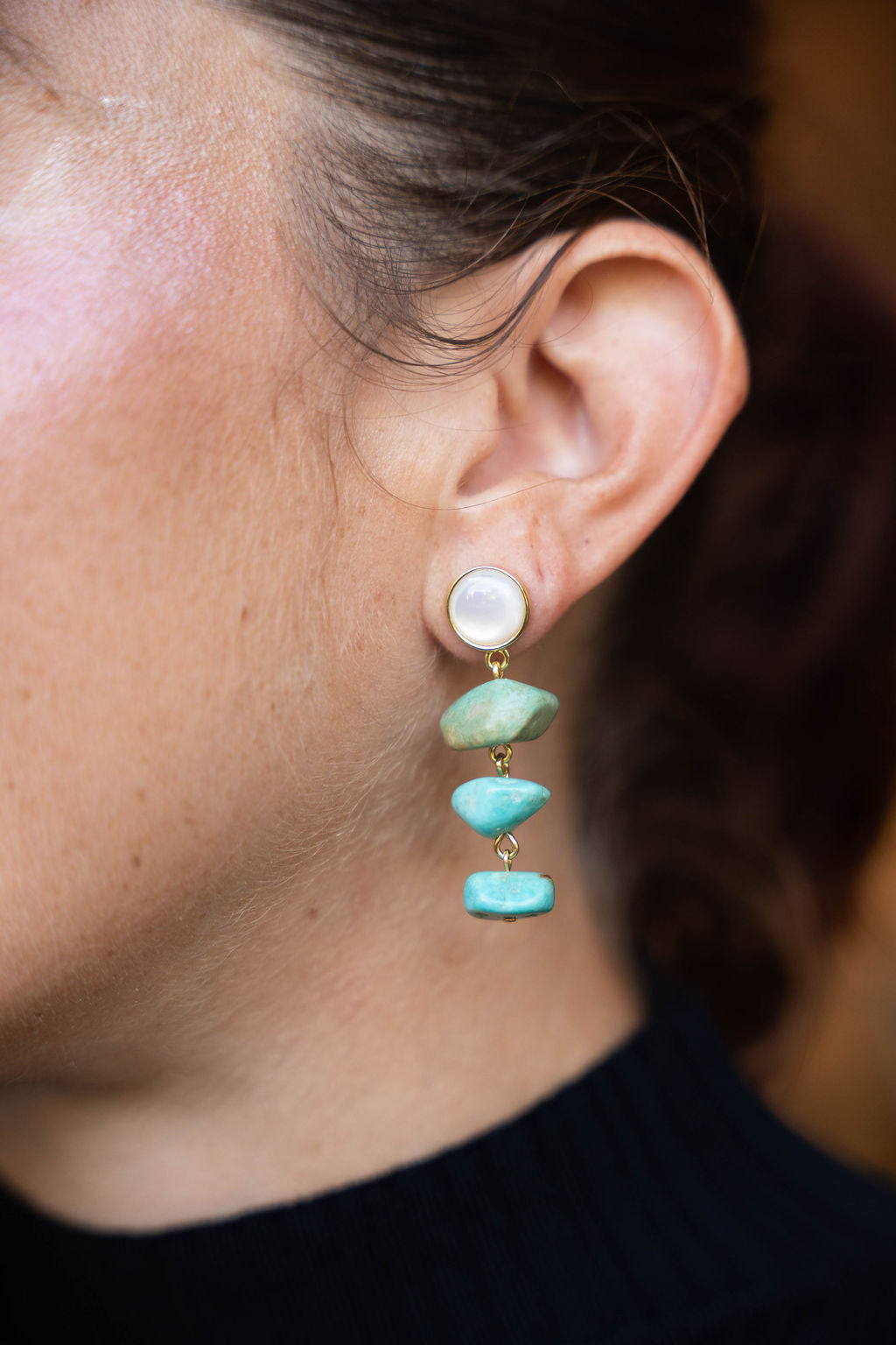 Close-up of an ear wearing a pearl and turquoise stone earring.