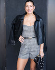 Woman in a plaid outfit with a black leather jacket standing against a dark background