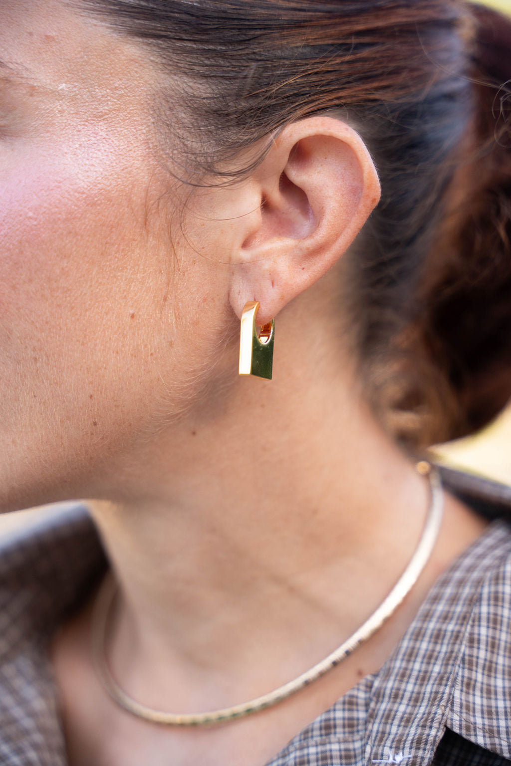 Close-up of a person wearing a gold hoop earring.