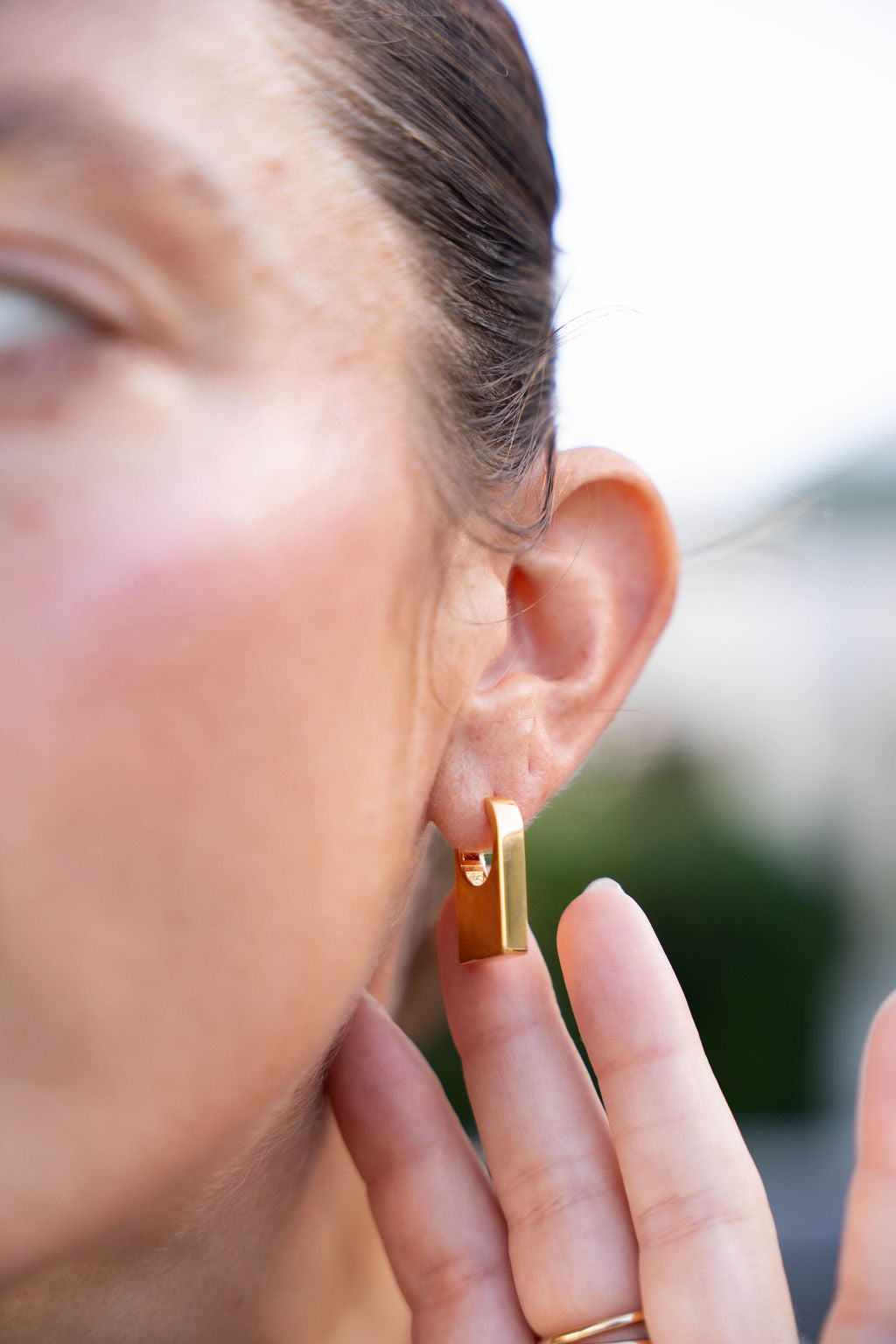 Close-up of a person wearing a gold earring with a blurred background