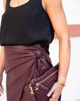 Person wearing a black sleeveless top and maroon skirt holding a matching clutch.