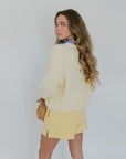 Woman wearing a light yellow sweater and skirt with a plain background