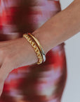 Gold bracelet on a wrist with a blurred red and white background