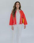 Woman wearing a red jacket and white pants with a yellow bag on a plain background