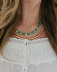 Close-up of a person wearing a gold and turquoise beaded necklace with a white blouse.