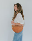 Woman holding an orange crossbody bag against a plain background