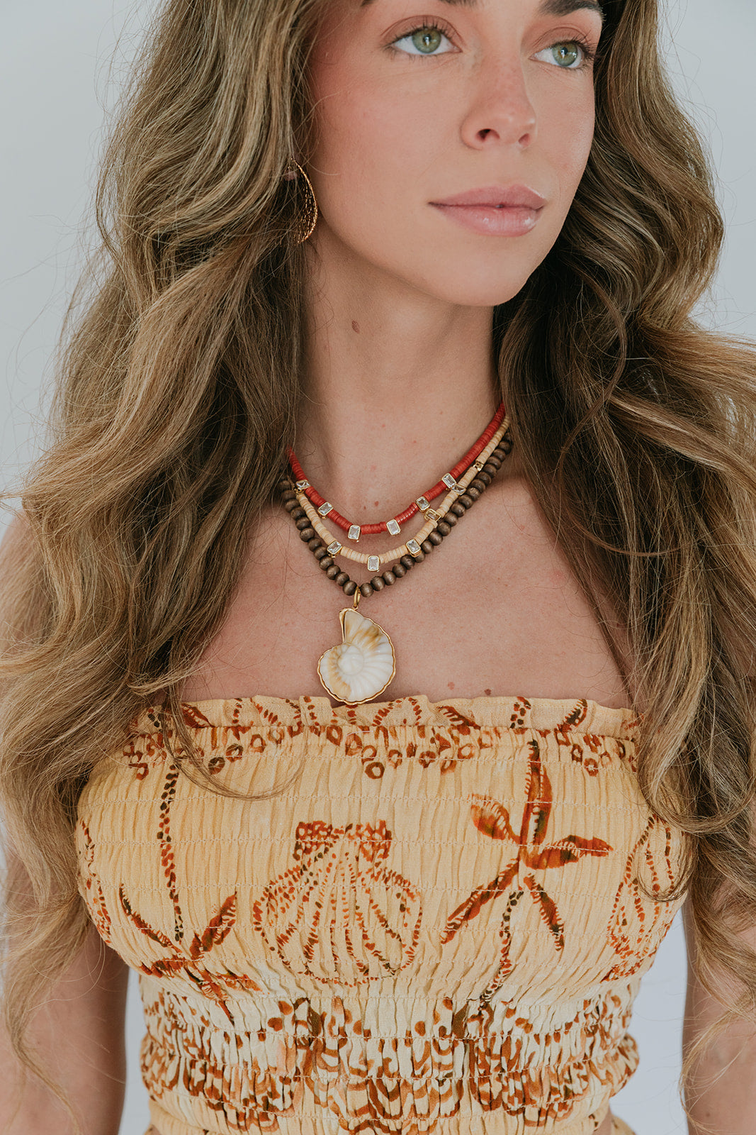 Woman wearing a top with shell designs and multiple necklaces against a white background