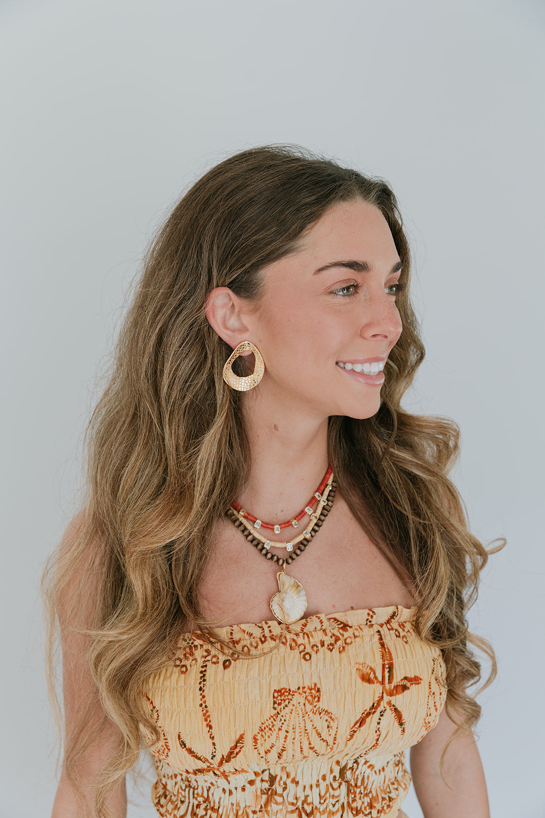 Woman wearing a decorative top and jewelry against a plain background