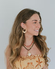 Woman wearing a decorative top and jewelry against a plain background