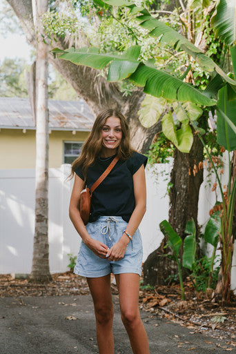 Woman standing outdoors with greenery and a building in the background