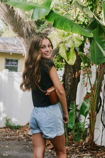 Woman standing outdoors with greenery and a white fence in the background, wearing Cancun Short Stripe. back view