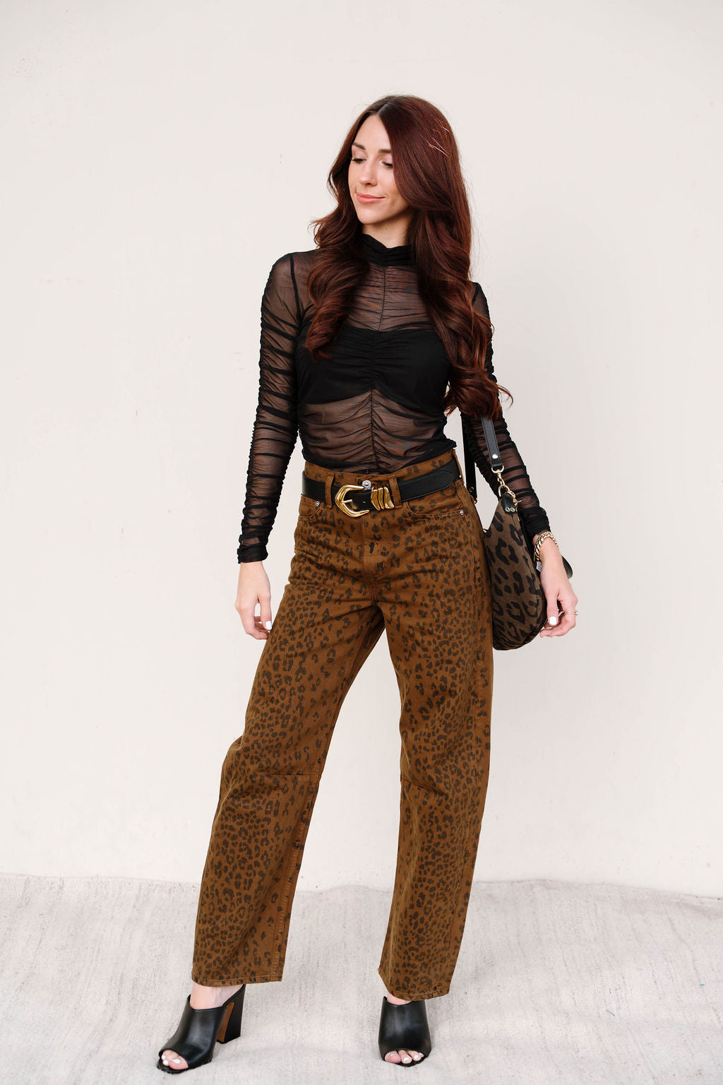 Woman wearing a black sheer top and brown patterned pants with a white background