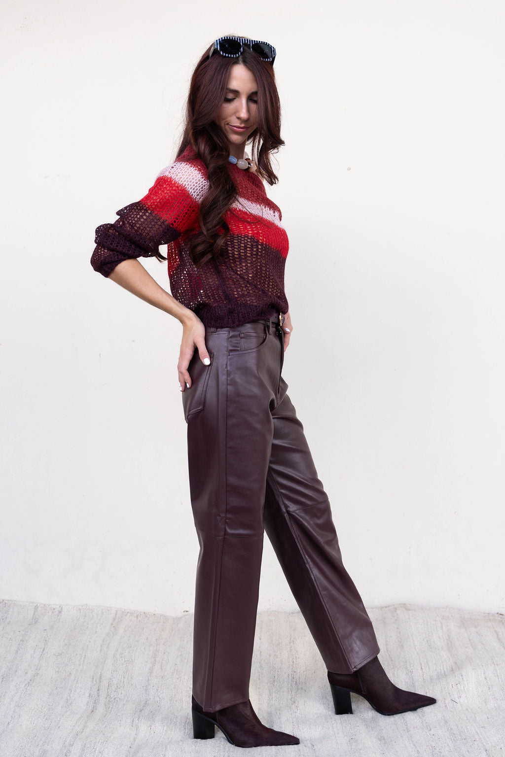 Woman wearing a colorful sweater and brown pants against a white background, side view