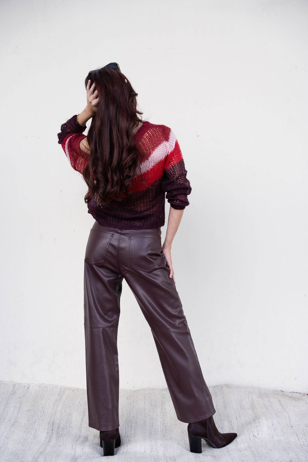 Person wearing a striped sweater and leather pants against a white background, back