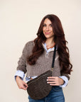 Woman wearing a brown sweater with a patterned bag on a plain background