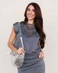 Woman wearing a gray dress holding a silver handbag against a plain background