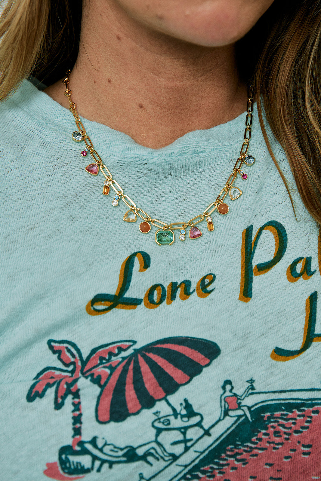 Person wearing a necklace with colorful beads, wearing a shirt with a palm tree and beach umbrella design.