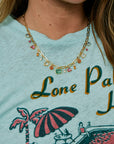 Person wearing a necklace with colorful beads, wearing a shirt with a palm tree and beach umbrella design.