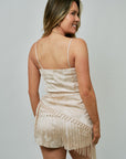 Woman wearing a beige fringe romper against a plain background, back view