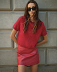 Woman wearing a red dress and sunglasses against a textured wall.