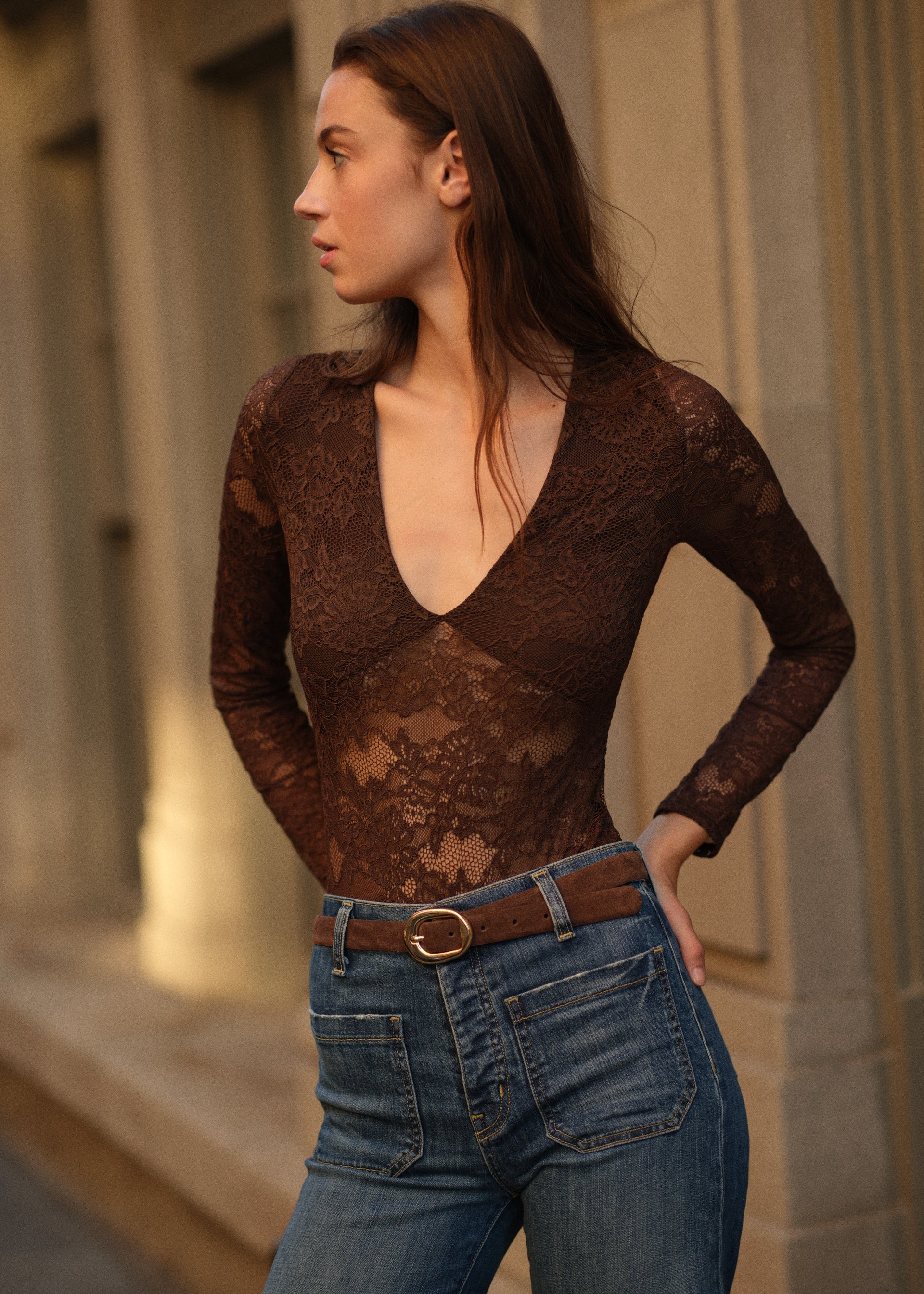 Woman wearing a sheer lace top and jeans standing outdoors.