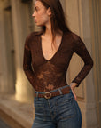 Woman wearing a sheer lace top and jeans standing outdoors.