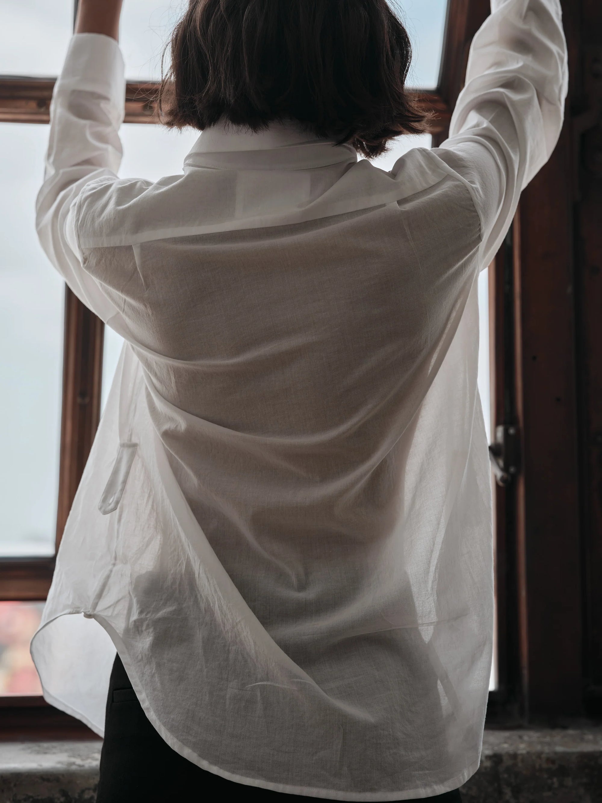 Person wearing a white shirt  with arms raised in front of a window