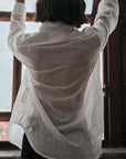 Person wearing a white shirt  with arms raised in front of a window