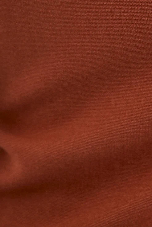 A close-up of a rust-colored knit fabric texture with soft folds and horizontal ribbing.