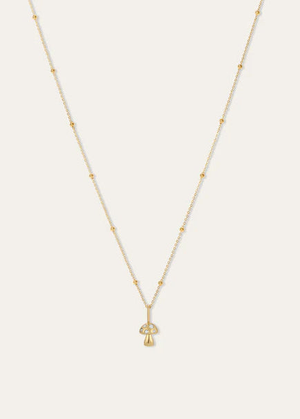 A delicate gold necklace with a small mushroom-shaped pendant, displayed against a solid off-white background.
