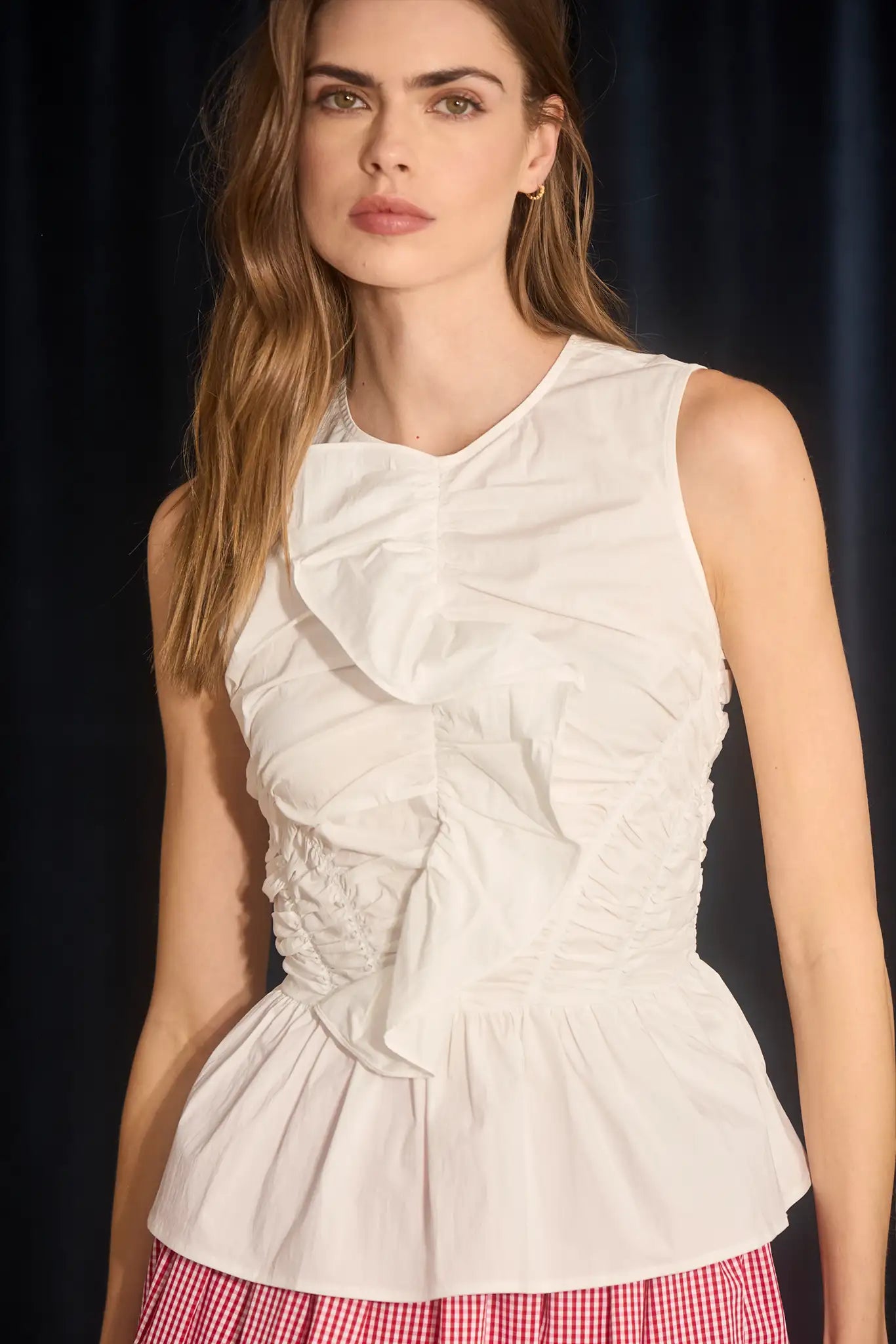 Woman wearing a white ruched top with a dark background
