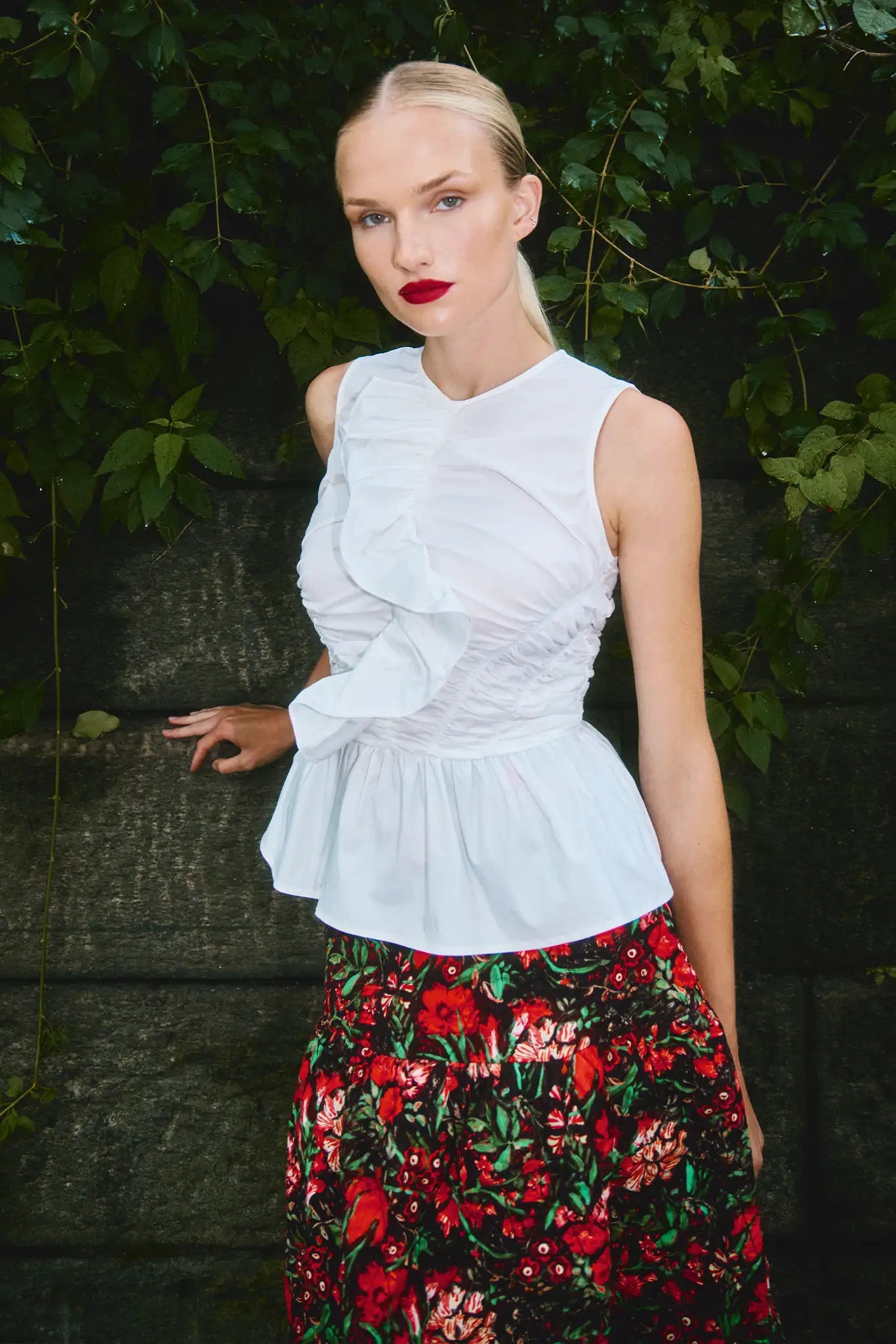 Woman wearing a white sleeveless top and red floral skirt against a natural background