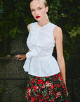 Woman wearing a white sleeveless top and red floral skirt against a natural background