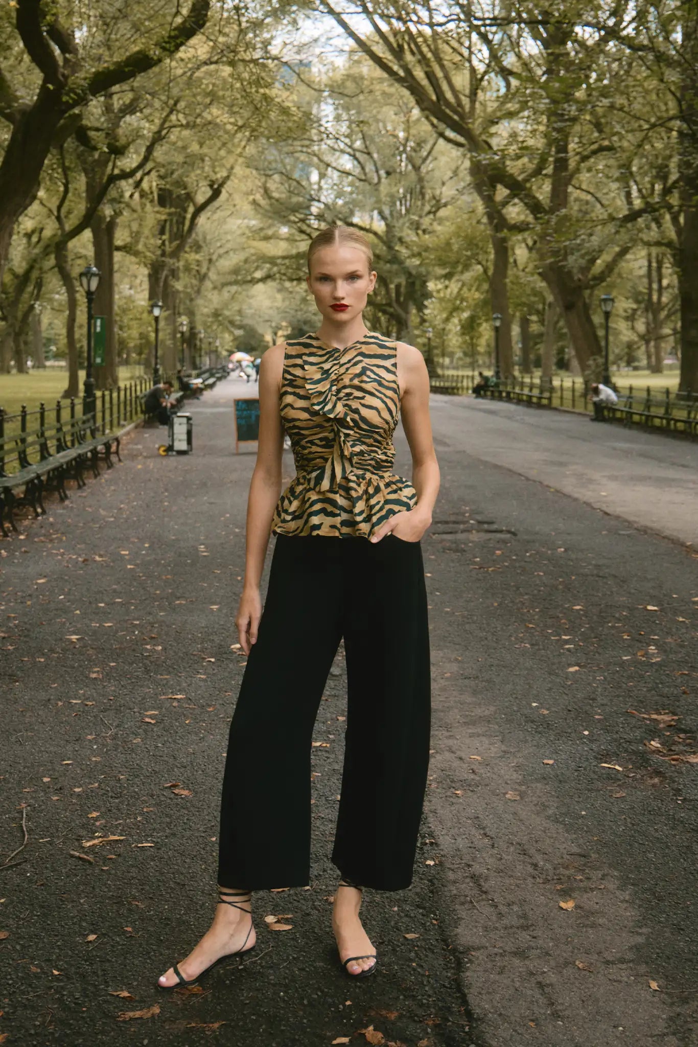 Woman in a park wearing a tiger-striped top and black pants.