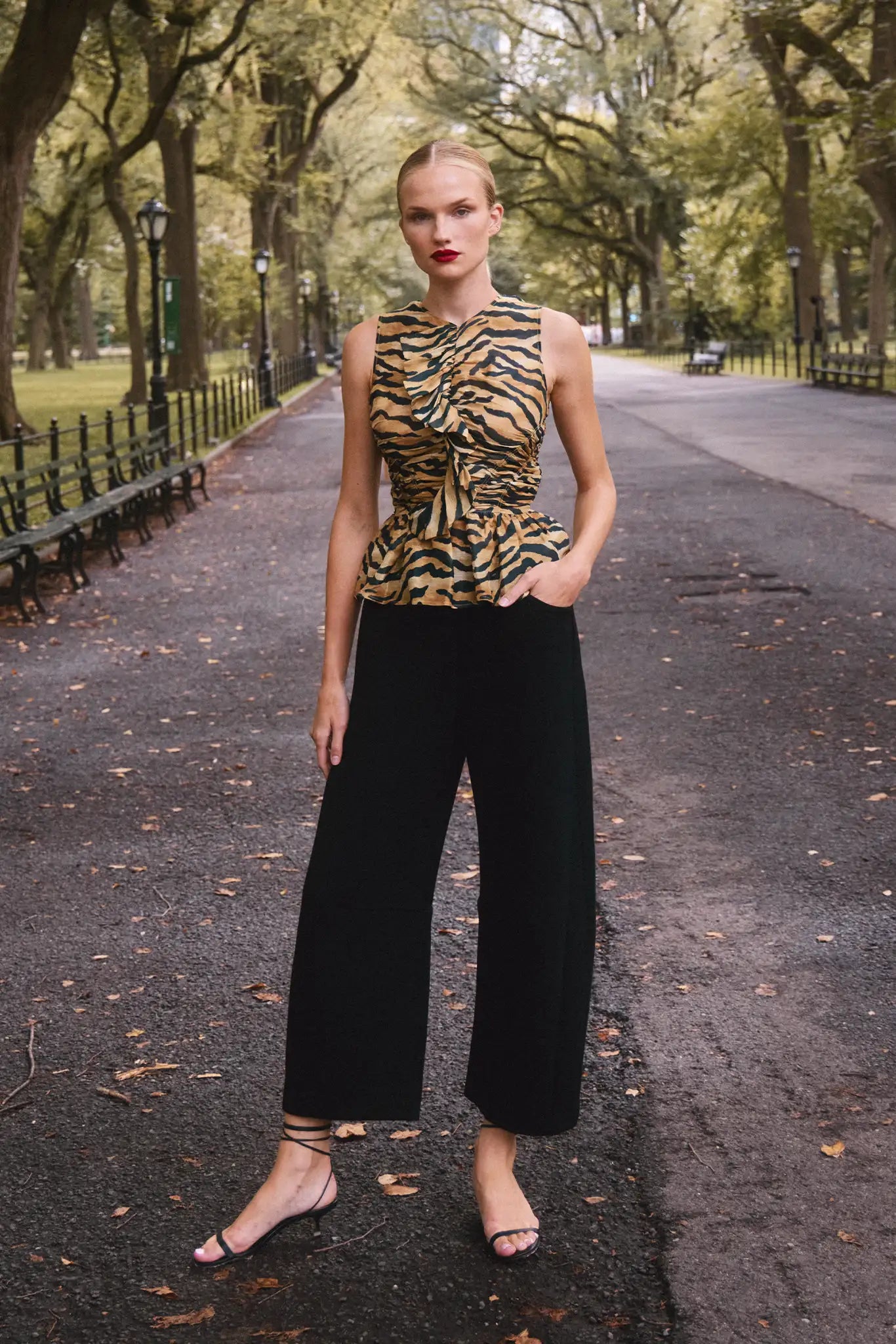 Woman in a leopard print top and black pants standing on a tree-lined street.