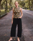 Woman in a leopard print top and black pants standing on a tree-lined street.