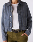 Person wearing a striped jacket over a white shirt with green pants on a plain background