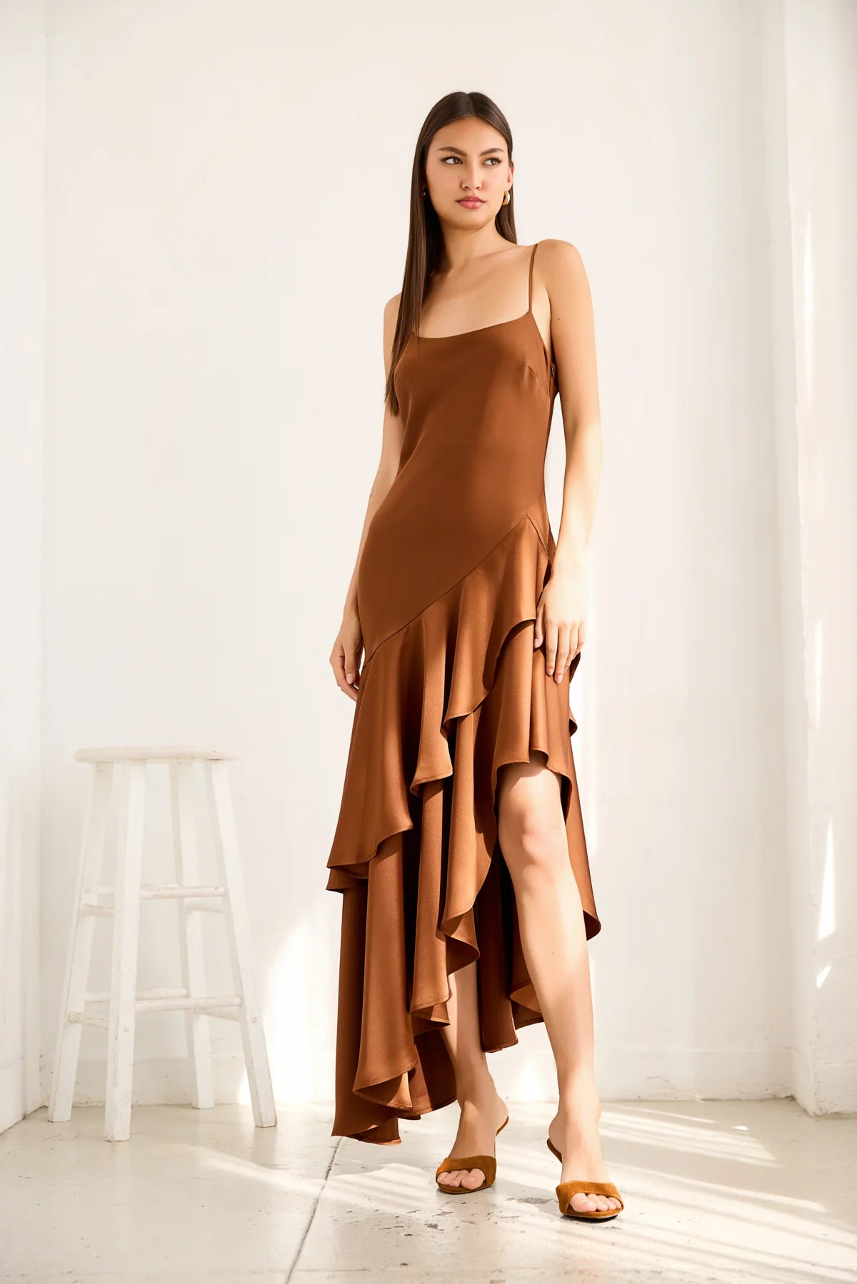 Woman wearing a brown dress with ruffled layers in a bright room.