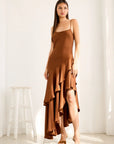 Woman wearing a brown dress with ruffled layers in a bright room.