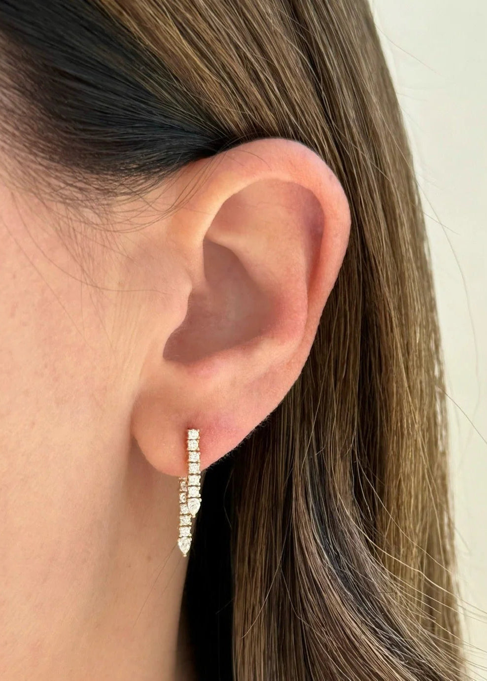Close-up of an ear wearing a diamond hoop earring with a neutral background