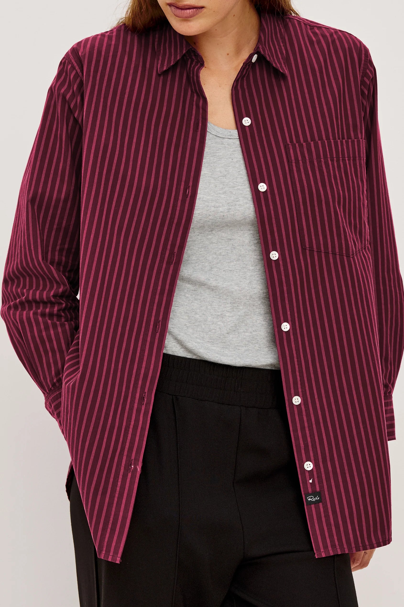 Person wearing a maroon and white striped shirt over a gray top and black pants on a light gray background front view
