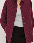 Person wearing a maroon and white striped shirt over a gray top and black pants on a light gray background front view