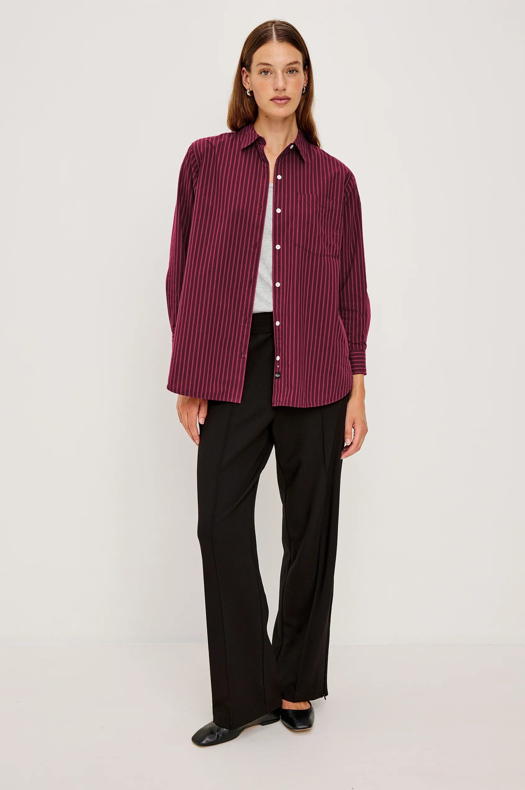 Woman wearing a burgundy striped shirt and black pants on a white background front view
