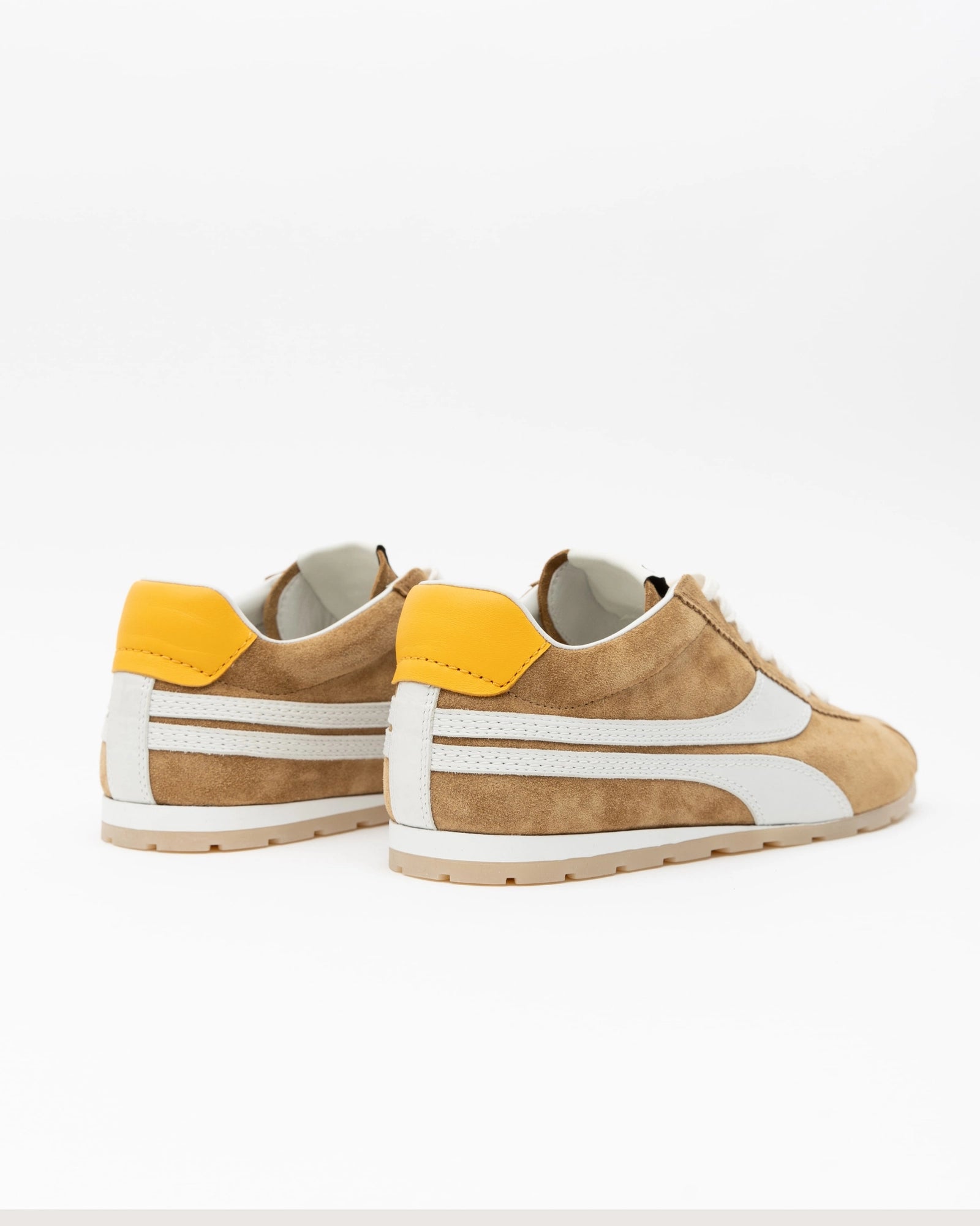 Pair of tan sneakers with yellow accents on a white background, back view