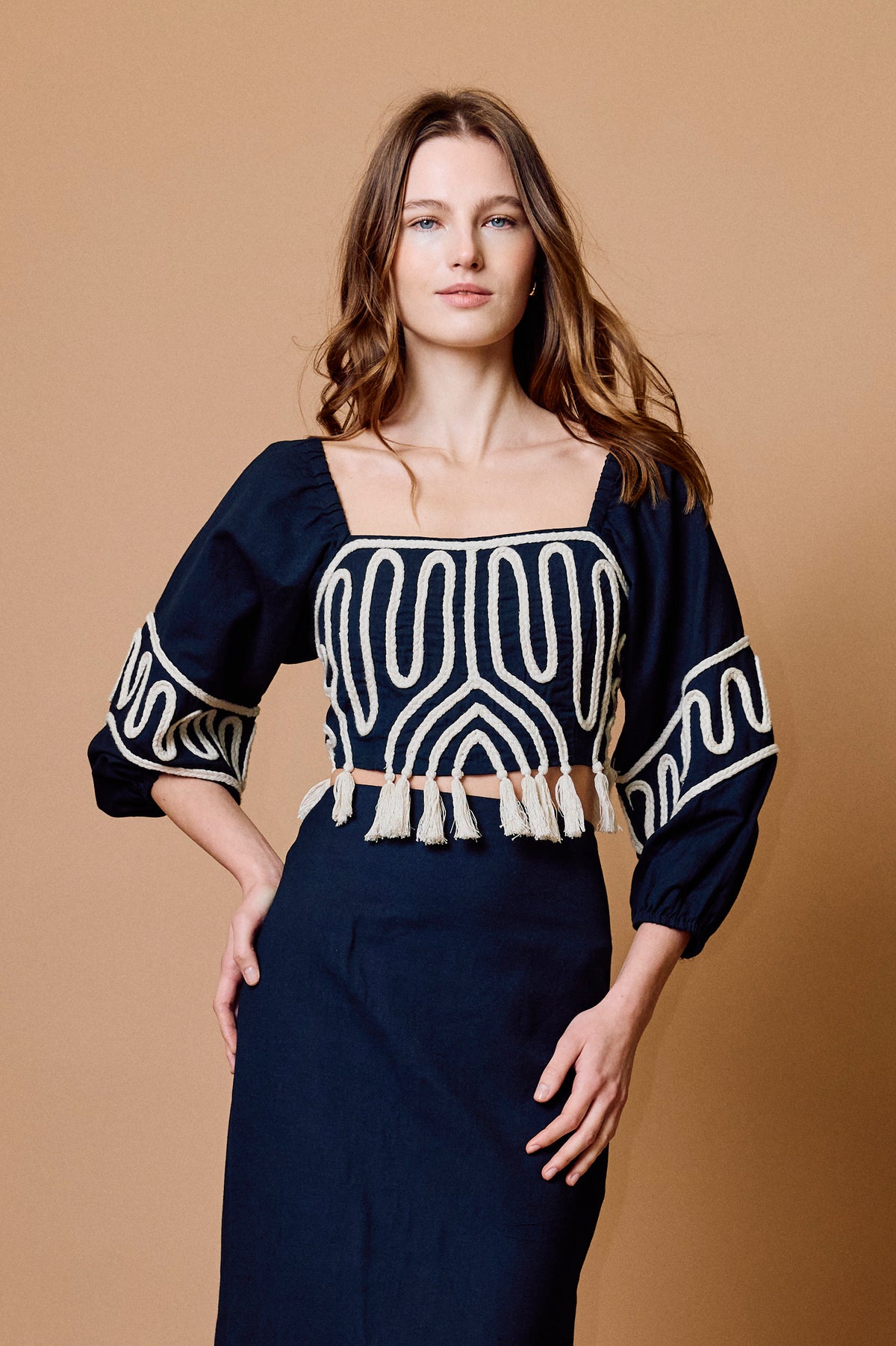 Woman wearing a black top with white patterns and a matching skirt against a brown background