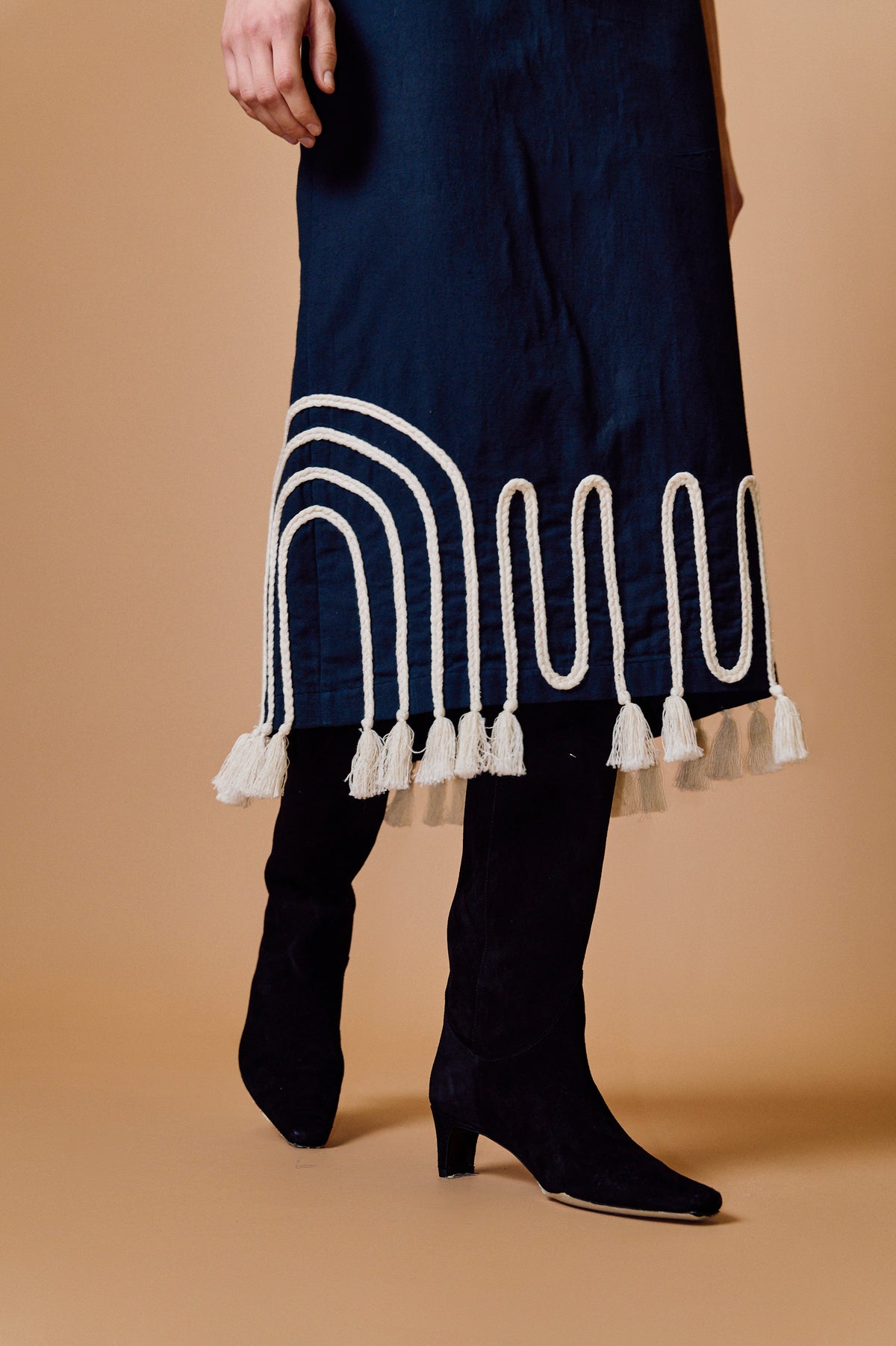 Black skirt with white decorative patterns and tassels worn by a person on a beige background